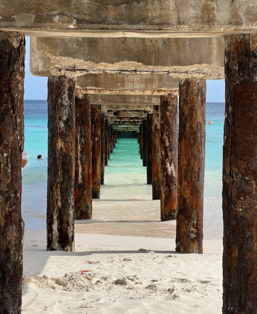 View beneath a weathered pier looking out to turquoise tropical water.